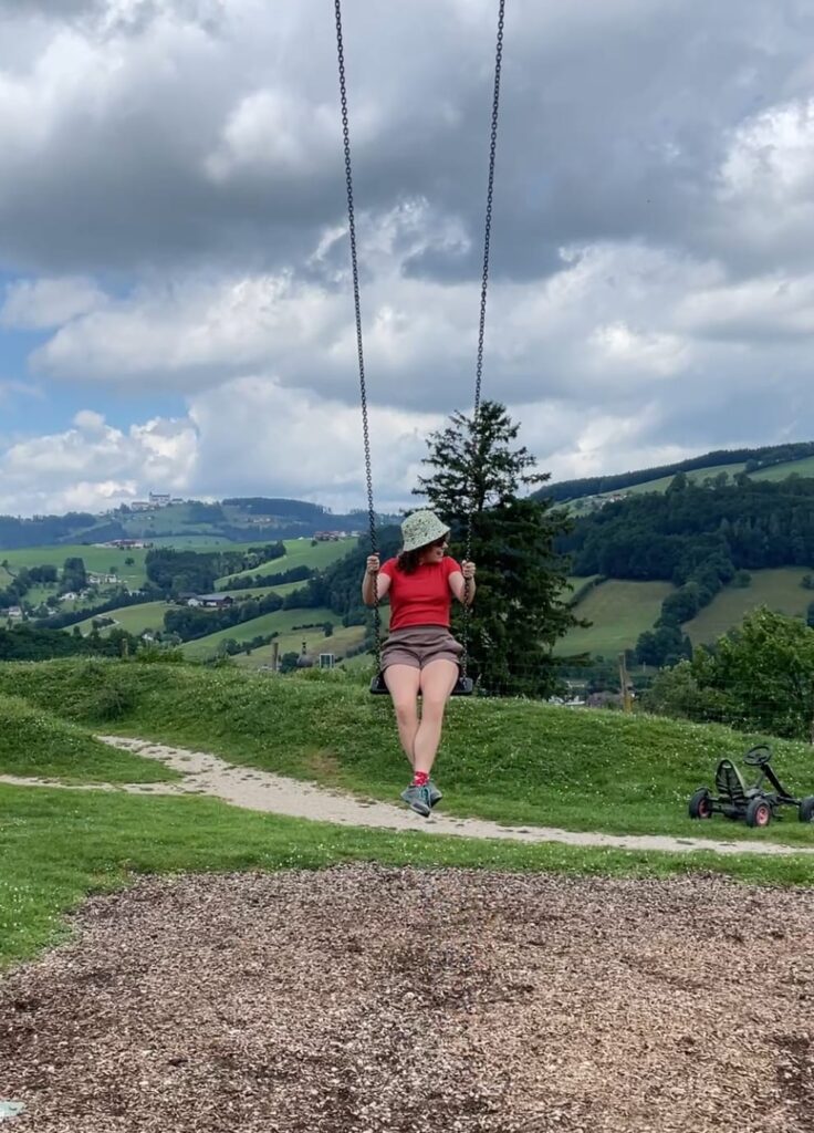 Julia sitzt auf einer Schaukel, im Hintergrund Berge.